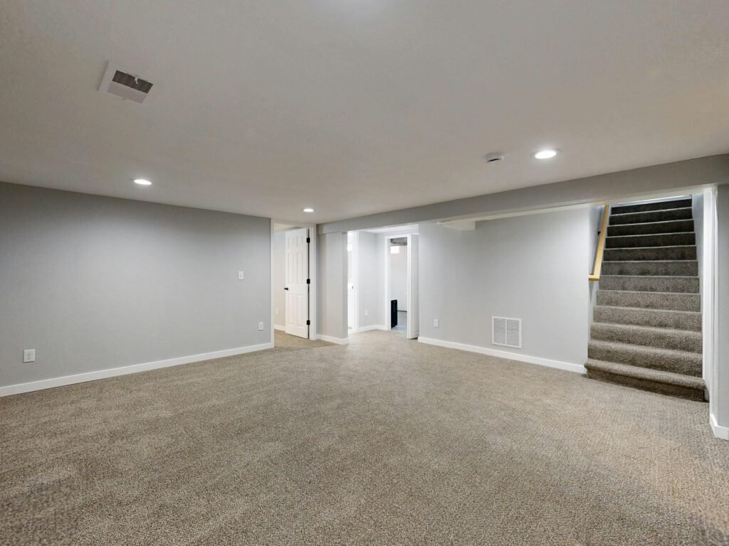 Empty modern basement with beige carpet and white walls, ideal for renovation.